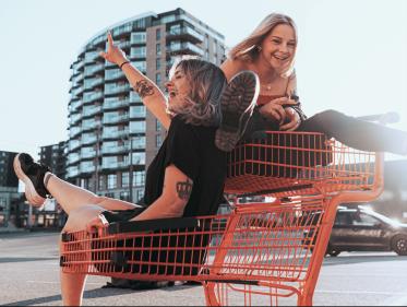 Two women sitting in a shopping cart with faces that make it clear they're saying; 'yaaaay!'